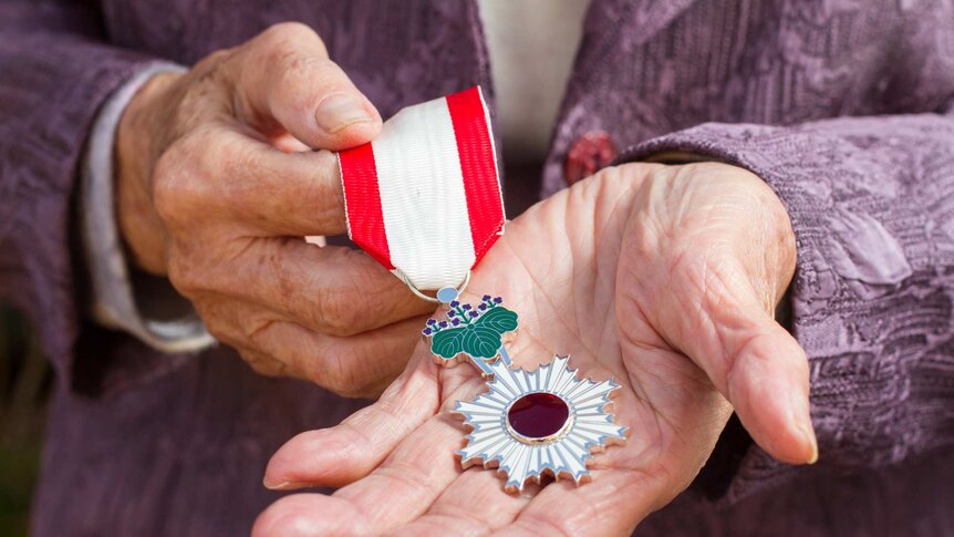 Older hands holding a medal with a red jewel in the centre