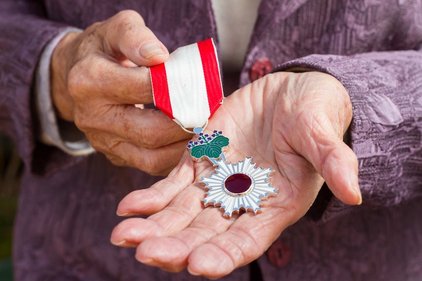 Older hands hold a medal with a red jewel in the center