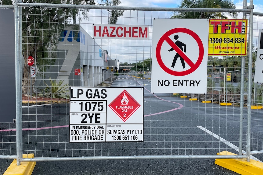 A fence adorned with hazard signs in front of a car park.