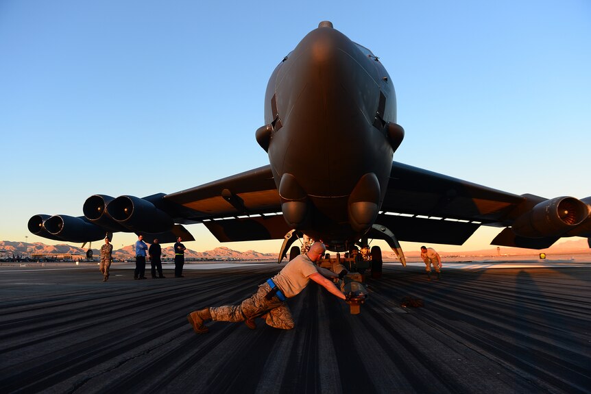 A photo taken looking up at a massive military aircraft. A soldier is pushing a tow bar towards its front wheel.