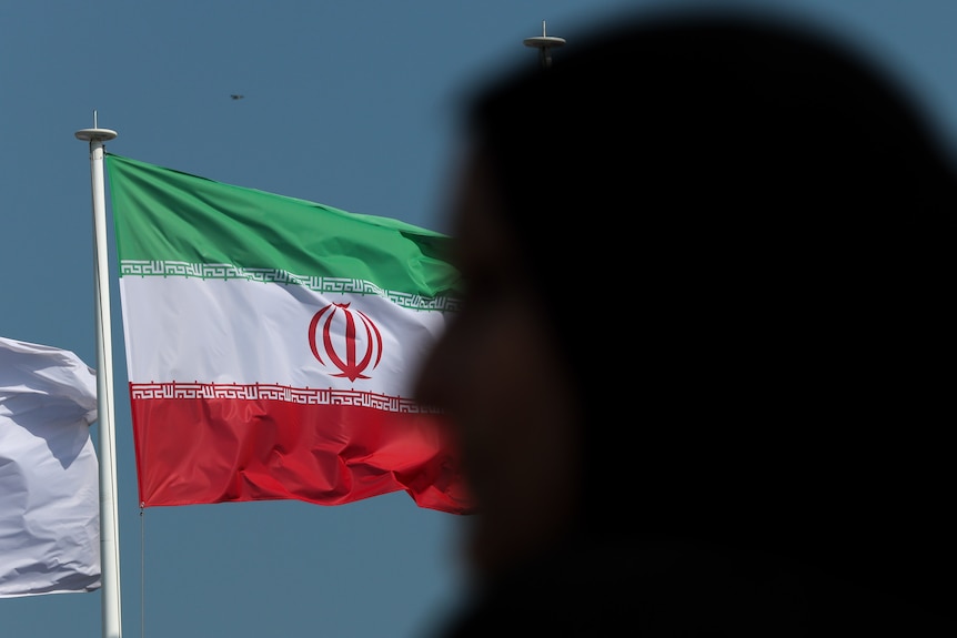 An image of the Iranian national flag flying with one side of it covered by a shadow.