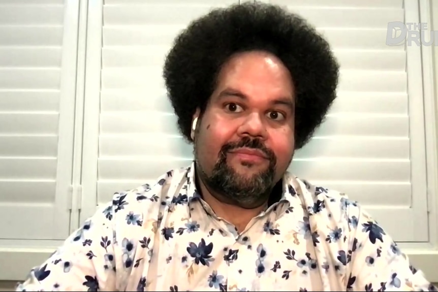 A man with a colourful shirt sits and looks toward a camera