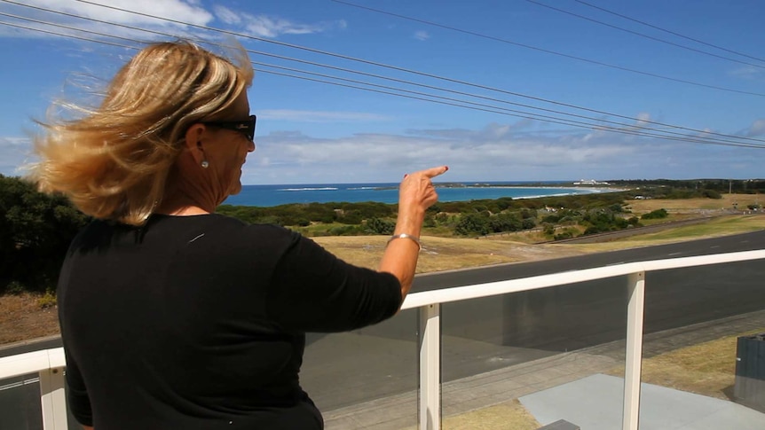 Woman pointing from her upper story balcony towards the nearby beach where she goes camping