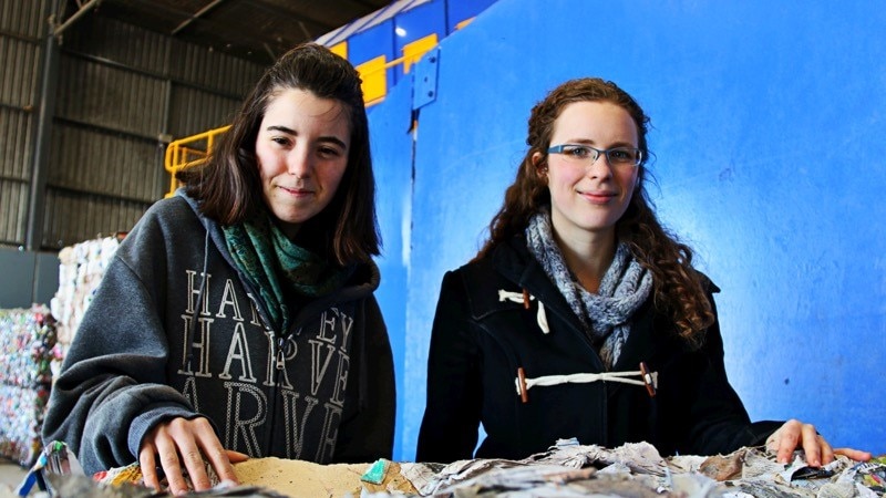Two young girls standing behind a cube of crushed recycled cardboard at Canberra's recycling centre.