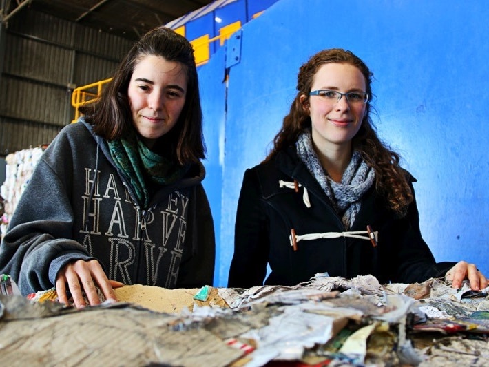 Two young girls standing behind a cube of crushed recycled cardboard at Canberra's recycling centre.