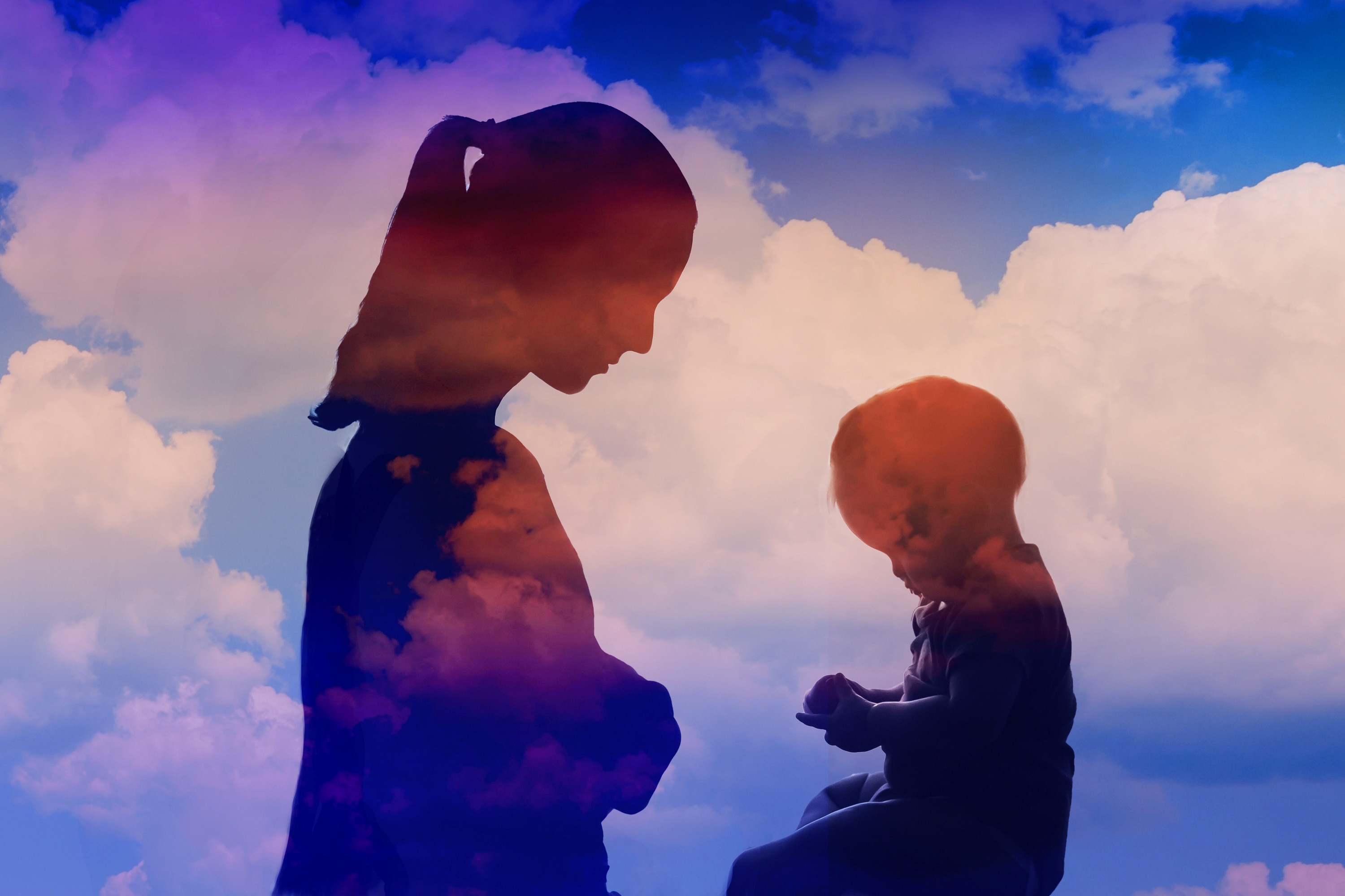 Silhouette of a woman and young child facing each other with clouds in the background