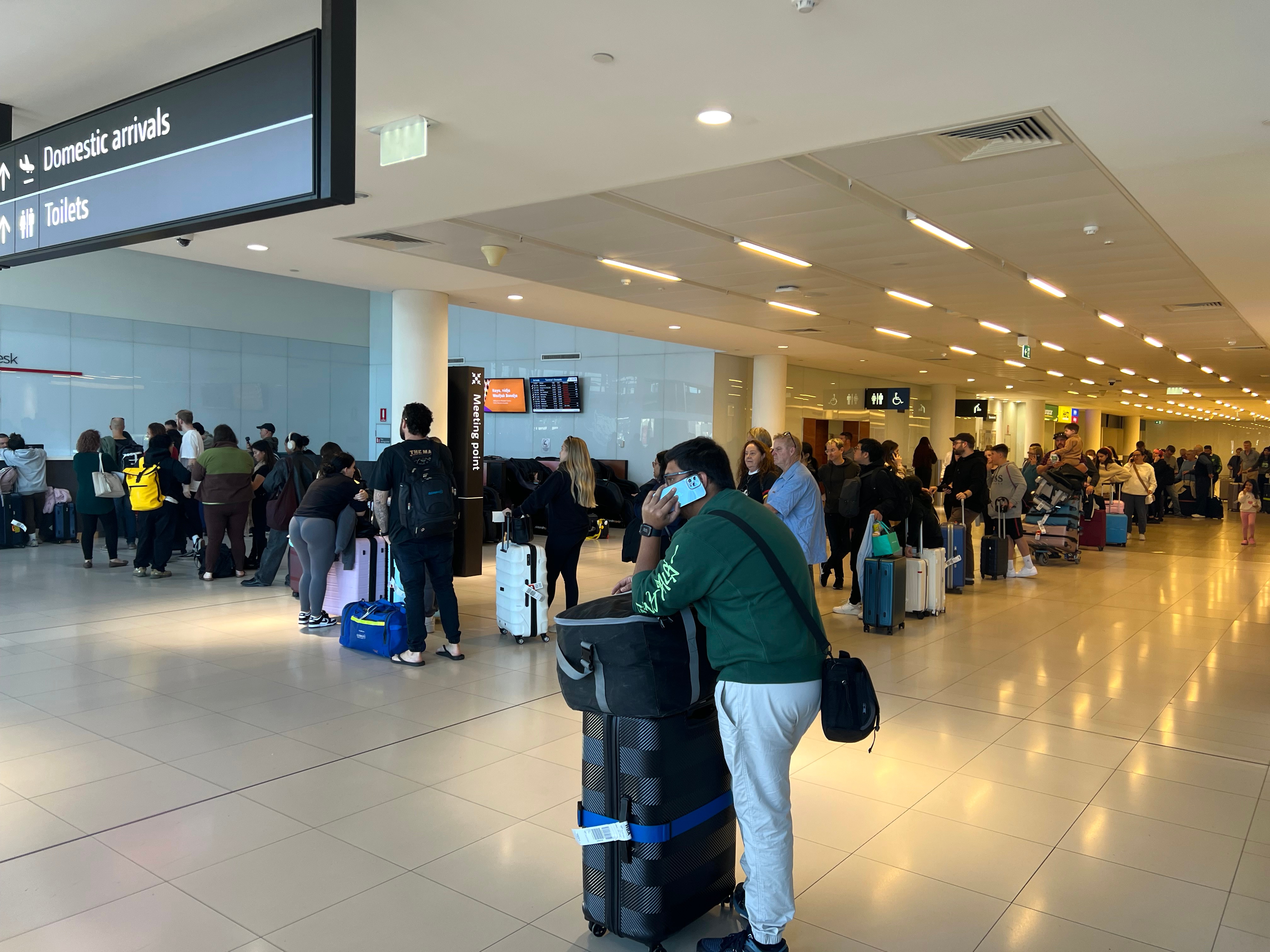 A long queue of people stand in line with their luggage at Perth Airport.