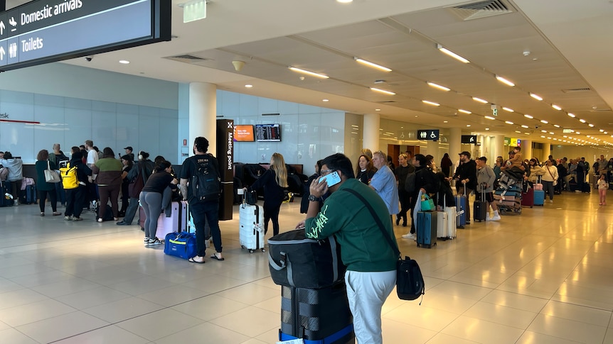 A long queue of people stand in line with their luggage at Perth Airport.