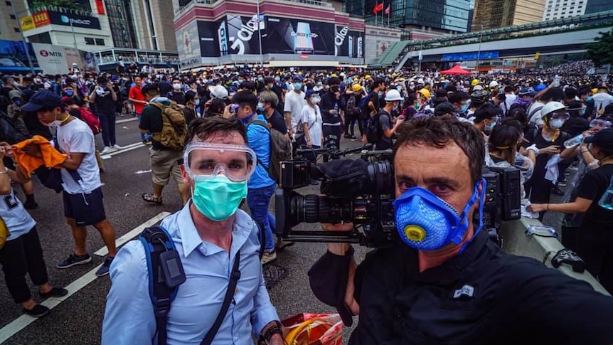 Birtles and Cumming wearing face masks standing in front of crowd of protesters in the street.