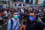 Birtles and Cumming wearing face masks standing in front of crowd of protesters in the street.
