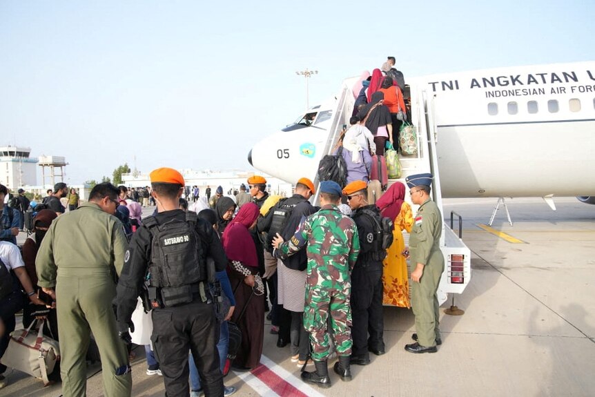 Indonesian citizens line up to board a plane in Sudan, as Indonesian military officers help.