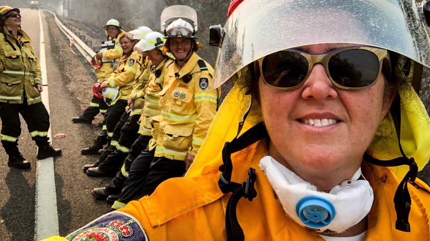 Selfie of woman in RFS uniform standing on side of road with firefighter colleagues smiling behind her.