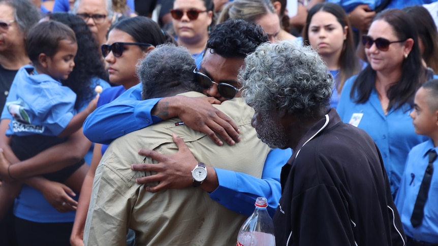 Two men hug among a crowd of people wearing blue. 