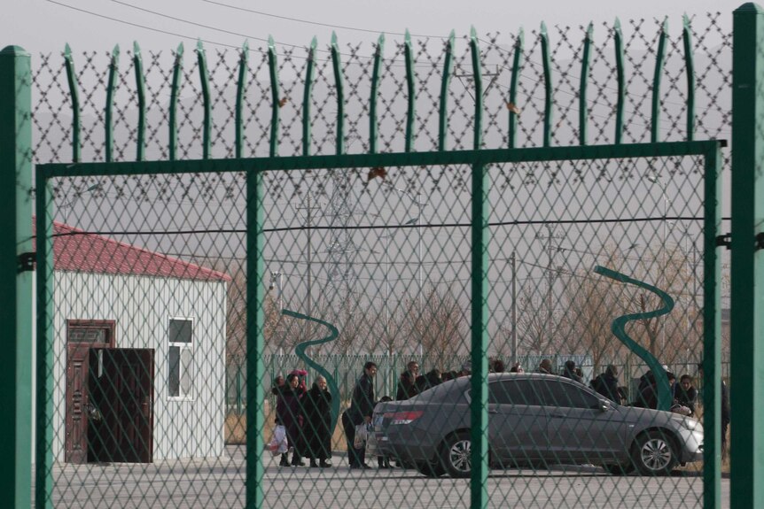 People line up at a so-called vocational skills education centre, surrounded by a barbed wire fence, in Xinjiang.