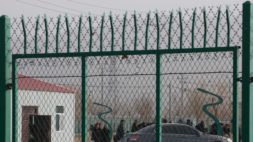 People line up at a so-called vocational skills education centre, surrounded by a barbed wire fence, in Xinjiang.