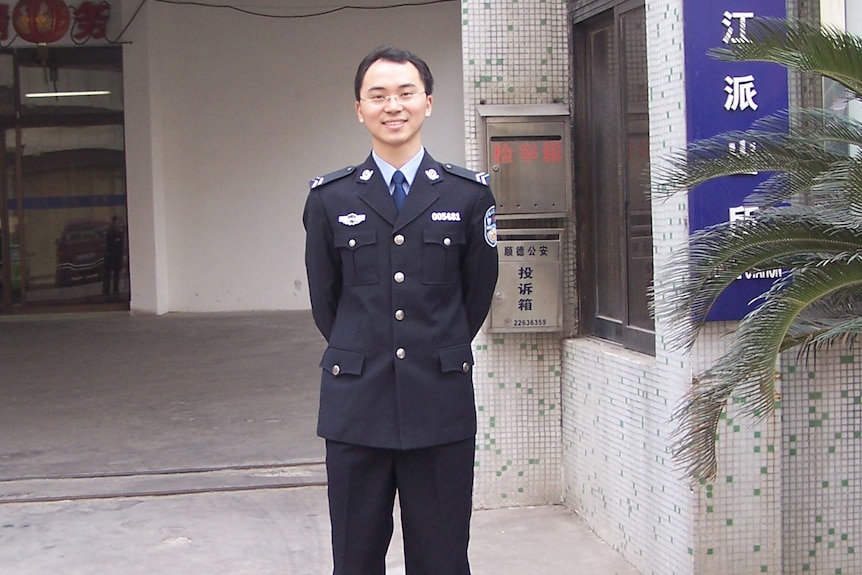 A man stands in a police officer's uniform, smiling at the camera. 