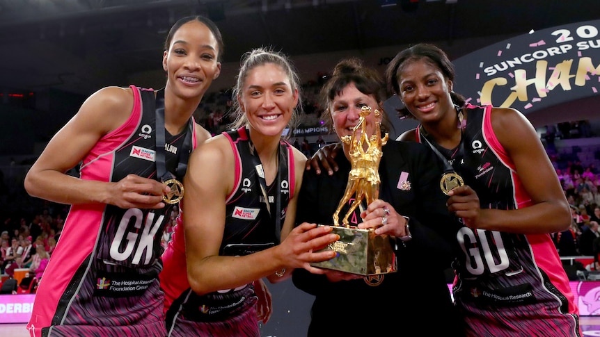 Defensive coach Cathy Fellows poses with the Super Netball trophy and her defenders