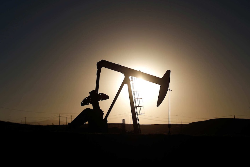 Silhouette of an oil derrick against the setting sun