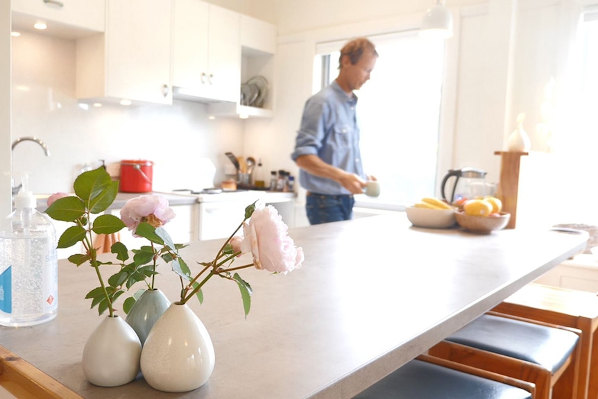 Andy Lemann holds a cup the kitchen with some roses in ceramic vases in the foreground.