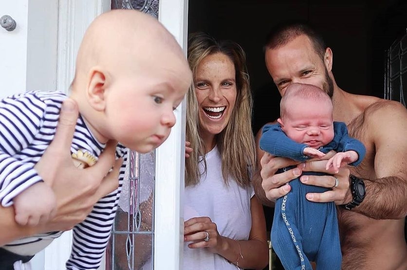 Parents introduce babies to each other on the doorstep of a house by holding them a safe distance apart.