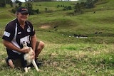 Eungella dairy farmer Dale Fortescue kneels down in his paddock.