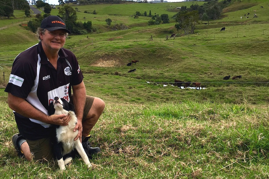 Eungella dairy farmer Dale Fortescue kneels down in his paddock.