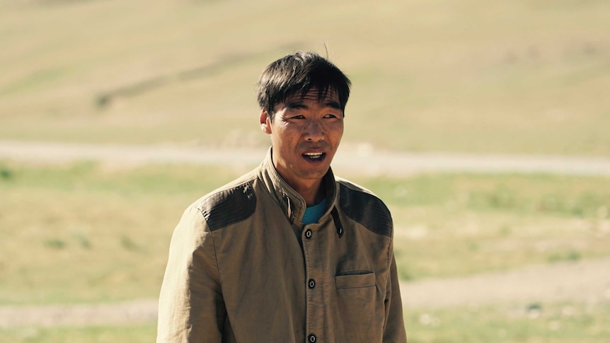 A Mongolian sheepherder stands with his hands in his pockets