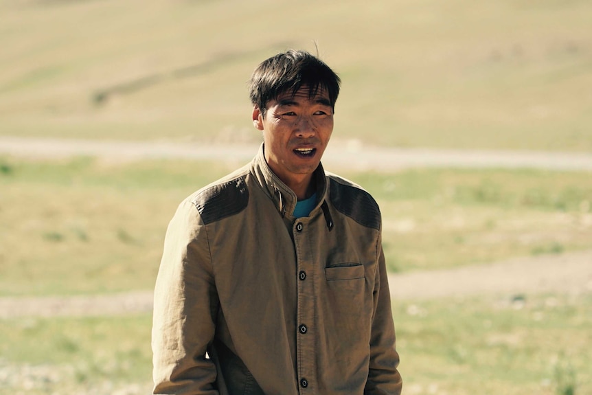 A Mongolian sheepherder stands with his hands in his pockets