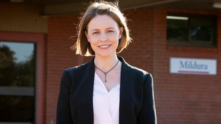 A young female politician with short brown hair and a navy jacket smiles at the camera.