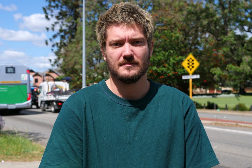A man in a green shirt stands in front of a main road