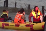 Three women wearing lifejackets sit in an inflatable SES dinghy.