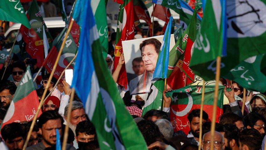 A portrait of Imran Khan is held up in a crow which is also holding flags 