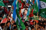 A portrait of Imran Khan is held up in a crow which is also holding flags 