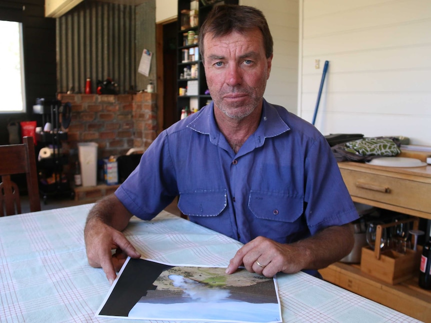 A man sits in his living room, holding a photo of a bushfire taken from a helicopter.