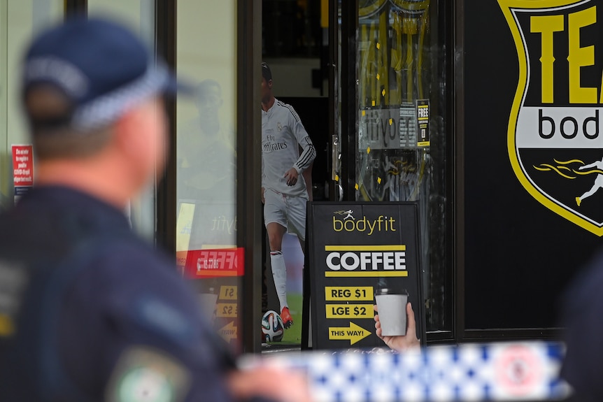 A police man stands outside a glass door covered with yellow stickers.