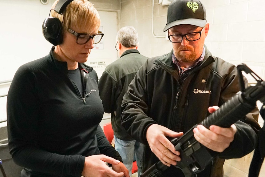 A man wearing a cap shows a woman how to hold an AR-15 rifle
