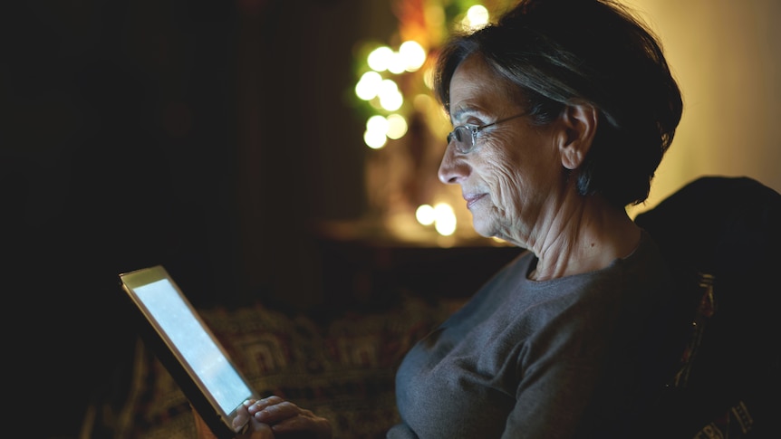 A woman sits in the dark looking at a laptop.