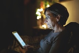 A woman sits in the dark looking at a laptop.