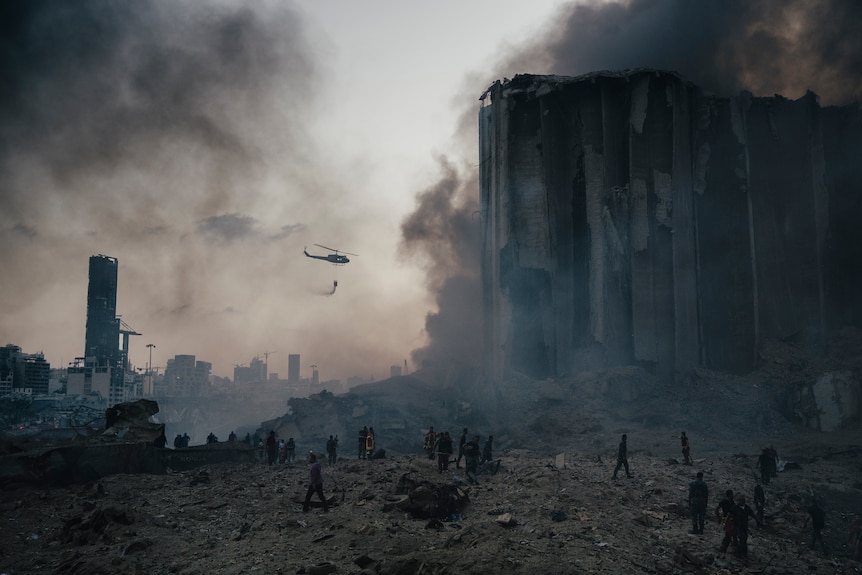 A helicopter makes a drop over a smoking building as firefighters work on the ground.