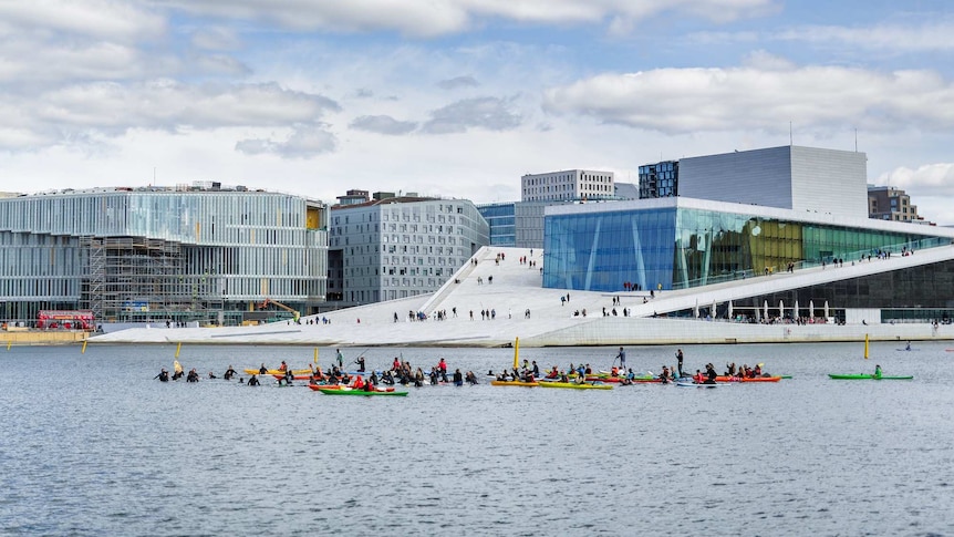 People on kayaks and paddleboards in the water in front of city buildings