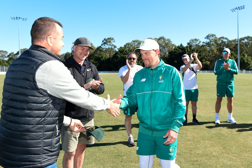 Two men shaking hands with people in the background clapping. 