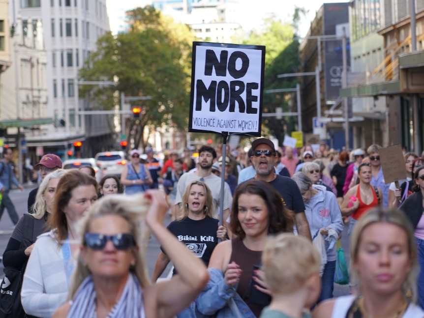 a gorup of people marching, a woman holds up a sign that says no more