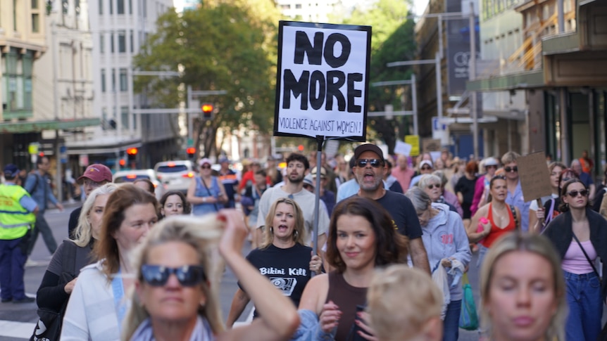 a gorup of people marching, a woman holds up a sign that says no more