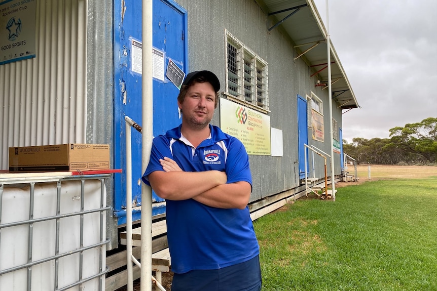 A man wearing a blue t-shirt and cap standing in front of a football club building.