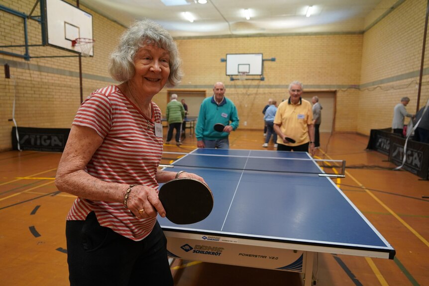 Three elderly people playing a game of table tennis