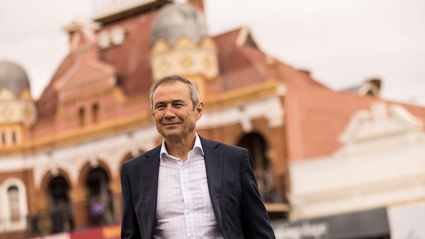 The WA Premier Roger Cook in a suit jacket and business shirt crossing the street in Kalgoorlie-Boulder