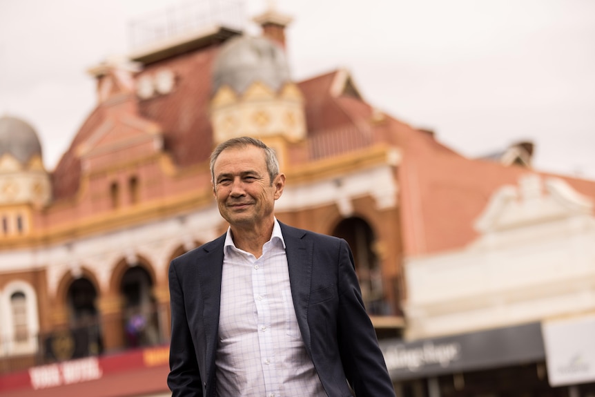 The WA Premier Roger Cook in a suit jacket and business shirt crossing the street in Kalgoorlie-Boulder