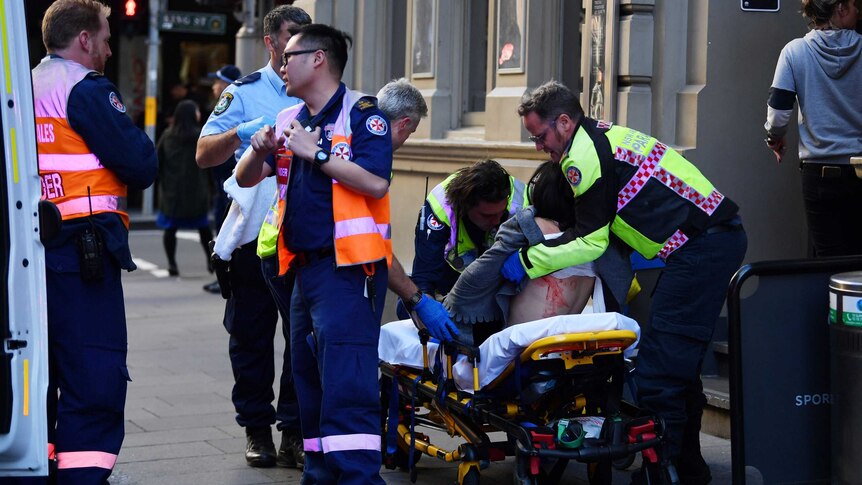 A woman is seen on a stretcher as paramedics tend to her and stand near her.