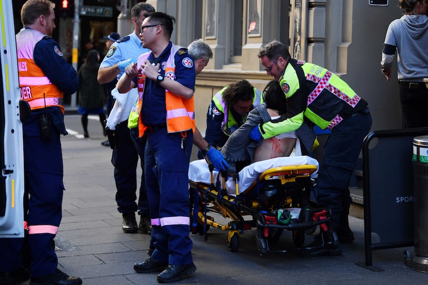 A woman is seen on a stretcher as paramedics tend to her and stand near her.
