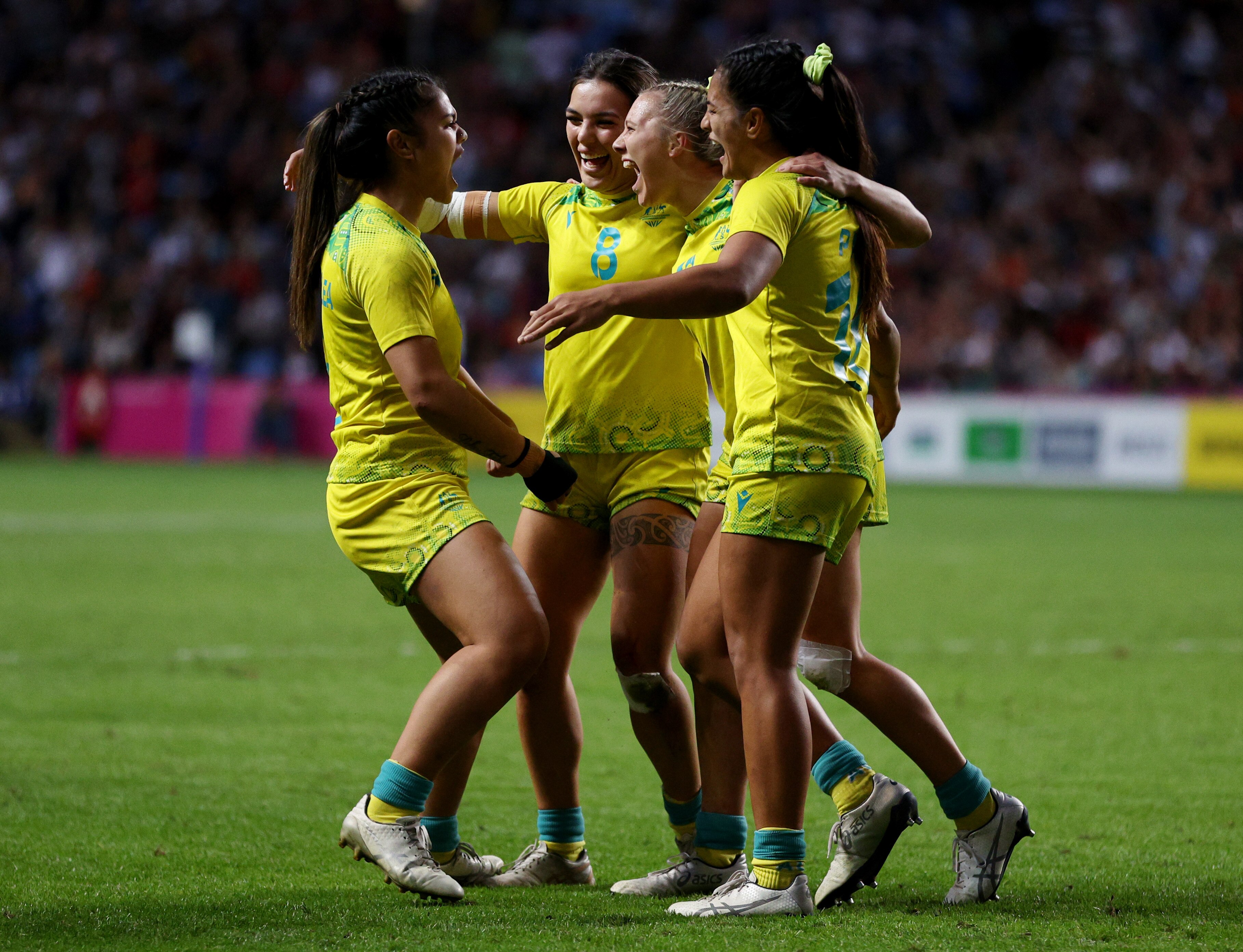 Four Australian women's rugby sevens players have a group hug in mid-pitch after winning Commonwealth Games gold.